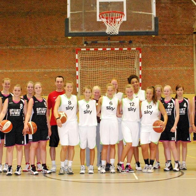 Gruppe von Basketballspielern in einheitlichen Trikots, die auf einem Basketballplatz posieren, mit Bällen in den Händen.