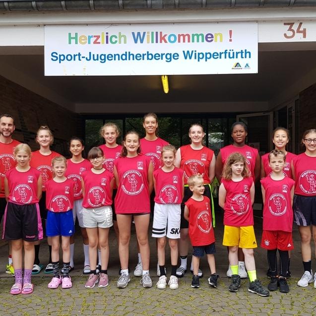 Gruppe von Kindern und Jugendlichen in roten T-Shirts vor einem Eingang mit „Herzlich Willkommen“-Schild, Sport-Jugendherberge Wipperfürth.