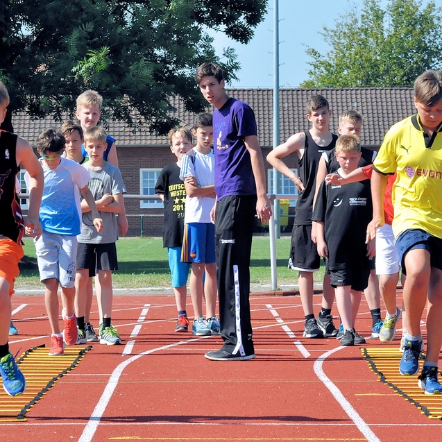 Gruppe von Jugendlichen trainiert auf einer Leichtathletikanlage, einige nutzen dabei Koordinationsleitern.