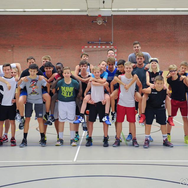 Gruppenshot von 24 Jungen in Sportbekleidung, die auf einem Basketballfeld stehen, einige auf den Schultern anderer.