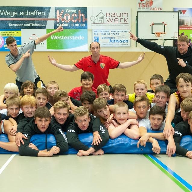 Gruppenszene von Jugendlichen und Trainern, die auf einer Matratze posieren, lächelnd und in Sportkleidung.