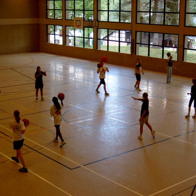 Gruppe von Menschen beim Basketballtraining in einer Halle, mehrere Spieler mit Bällen in der Hand.