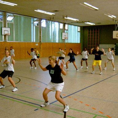 Gruppe von Mädchen und Jungen beim Sport in einer Halle, die gemeinsam Übungen im Fitnessbereich ausführen.