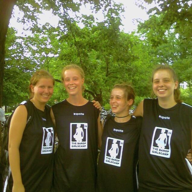 Vier Mädchen in schwarzen Trikots stehen lächelnd unter Bäumen, mit Logo des TVE Barop Girlscamps auf den Shirts.