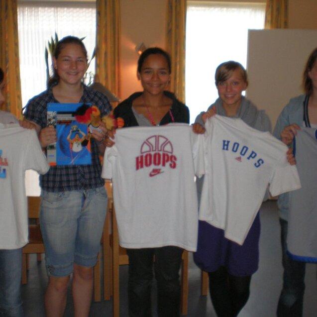 Fünf Jugendliche halten Basketball-T-Shirts in der Hand und zeigen ein Spielzeug sowie eine Broschüre.