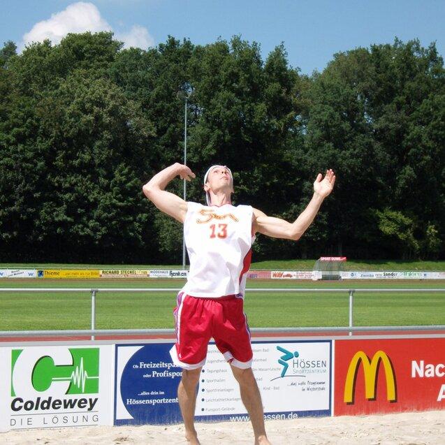 Mann im Sand hebt einen bunten Volleybal über den Kopf, um ihn im Beachvolleyballspiel zu schlagen.