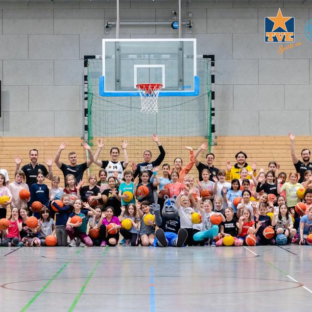 Gruppenschnappschuss von Kindern und Trainern in Sportkleidung, die mit Basketballen in einer Halle posieren.