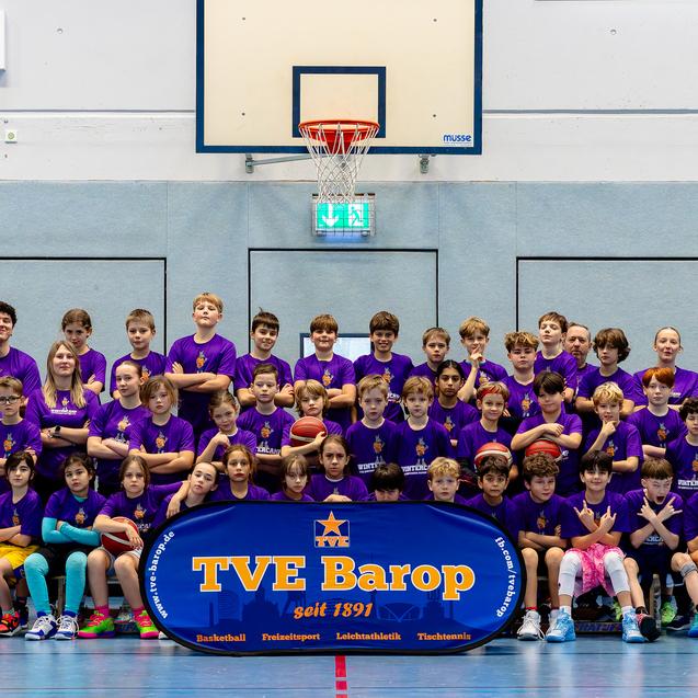 Gruppenshot von Kindern und Jugendlichen in lila T-Shirts auf einem Basketballfeld mit TVE Barop Banner.