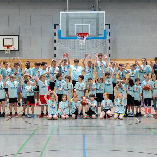 Gruppenshot von Kindern und Trainern in Sportkleidung, die in einer Basketballhalle posieren und Basketball halten.