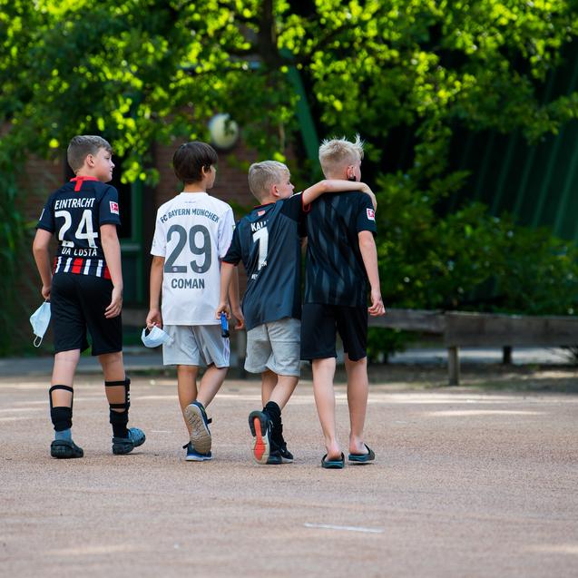 Vier Kinder in Fu&szlig;balltrikots gehen gemeinsam auf einem schattigen Platz.