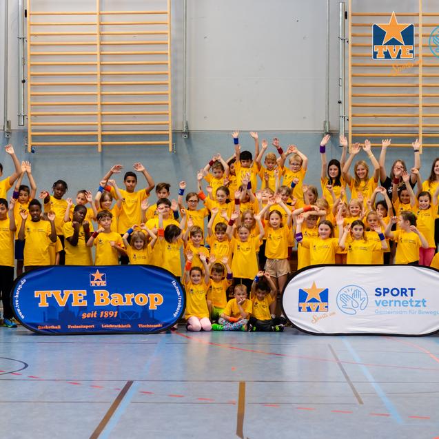 Gruppenszene von Kindern und Erwachsenen in gelben T-Shirts, die fröhlich in einer Sporthalle posieren.