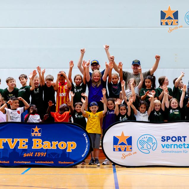 Gruppe von Kindern und Erwachsenen mit Jubelpose vor Banner von TVE Barop und SPORT vernetzt in einer Sporthalle.