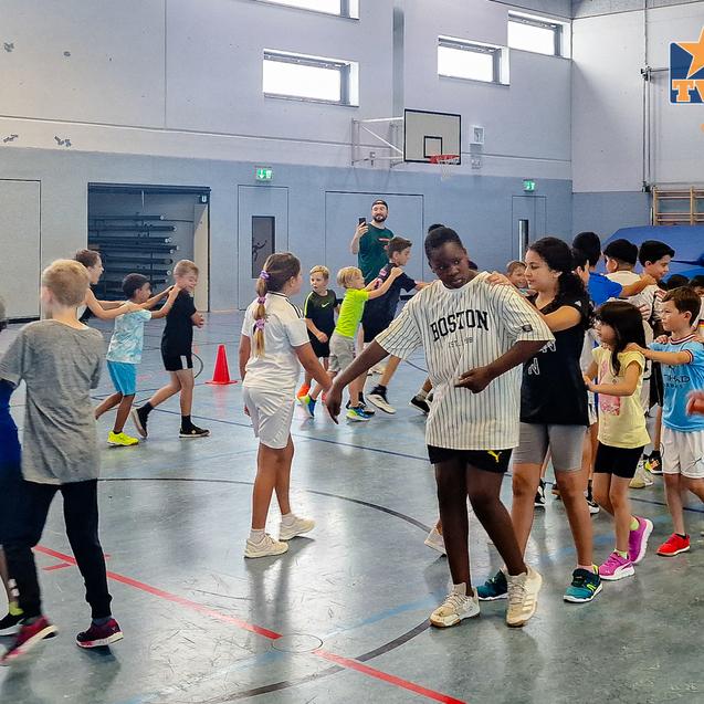 Gruppenspiel von Kindern in einem Sportraum, die zusammen in einer Reihe tanzen und interagieren.