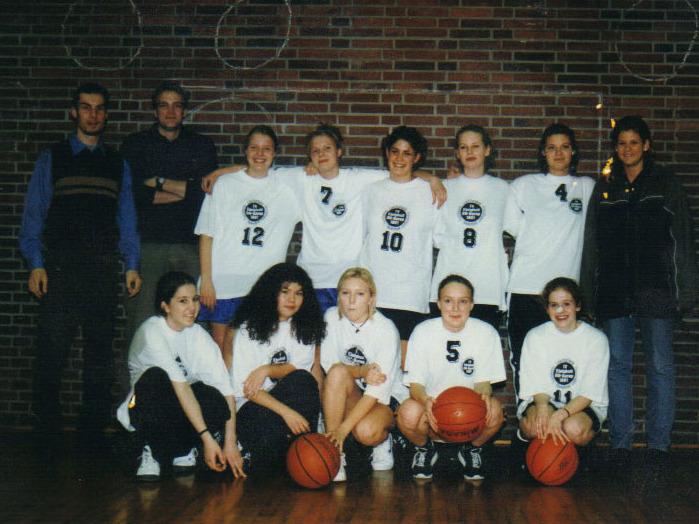 Mädchen 1998 Gruppenfoto einer Basketballmannschaft mit zehn Spielerinnen in weißen Trikots und zwei Trainern vor einer Ziegelwand.