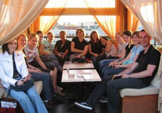 Gruppe von zwölf Personen sitzt in einem hellen Raum mit Vorhängen und Blick auf die Stadt.