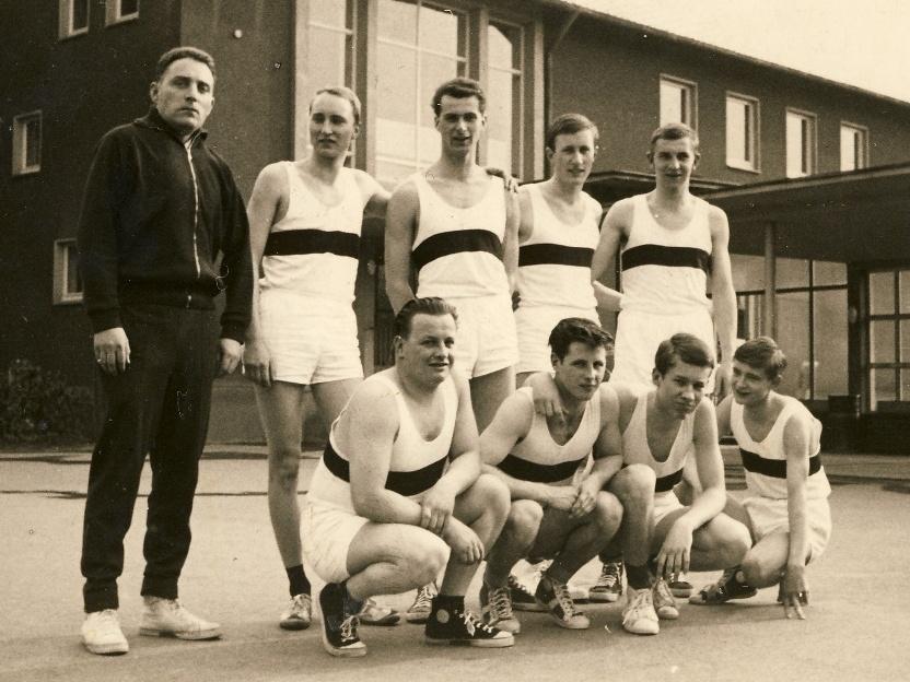 Gruppennfoto von neun Athleten in Sportkleidung, aufgenommen vor einem Gebäude, datiert 1962-63.