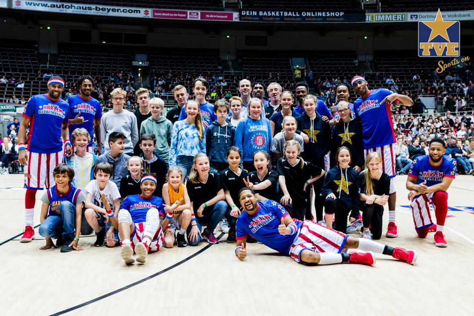 Harlem Globetrotters 2018 Gruppenfoto von Harlem Globetrotters und Fans auf einem Basketballfeld, mit lächelnden Gesichtern und sportlicher Kleidung.