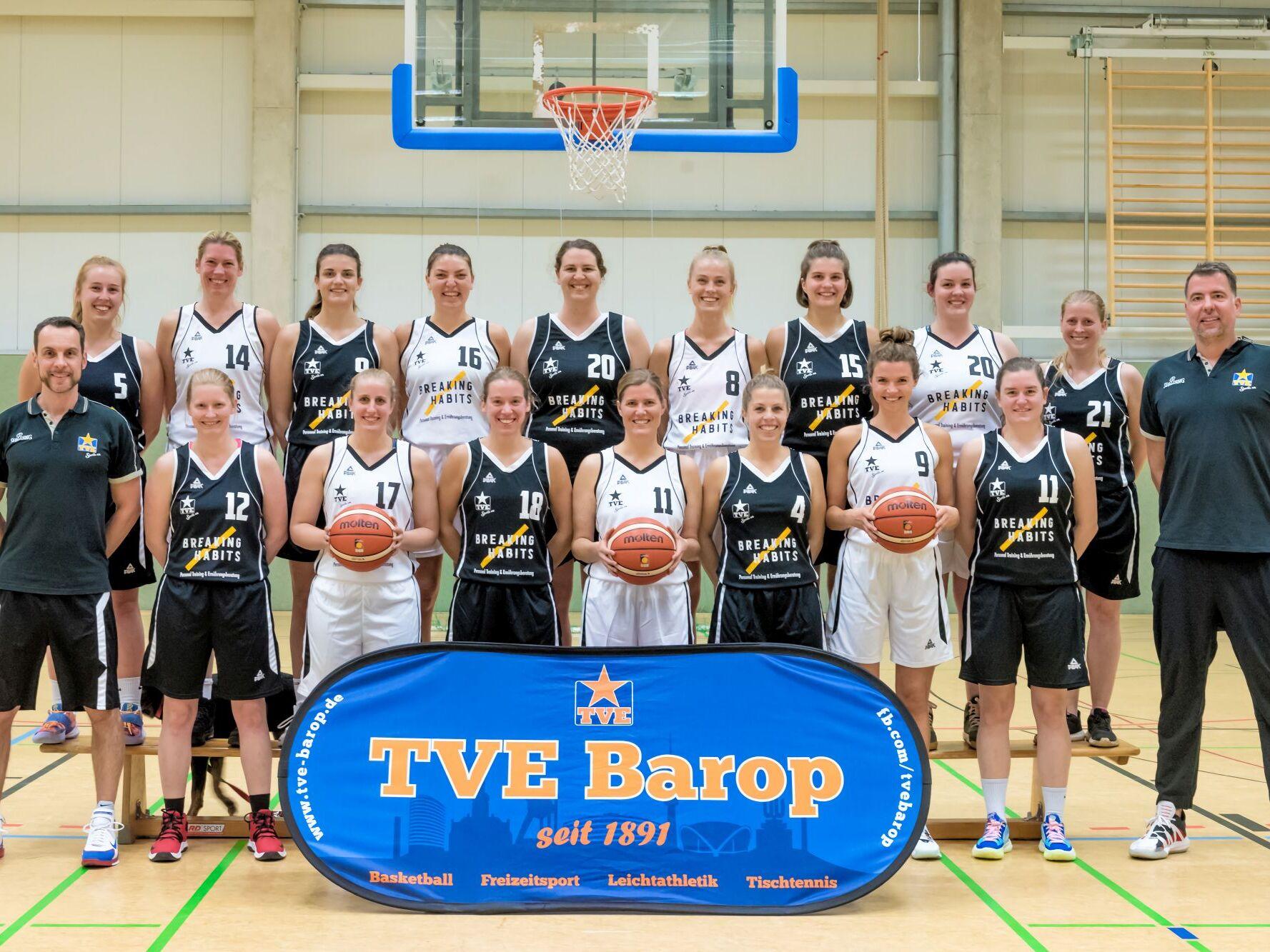 1. Damen 2021 Mannschaftsfoto einer Basketball-Mannschaft mit Spielerinnen in schwarzen und weißen Trikots vor einem Korb.