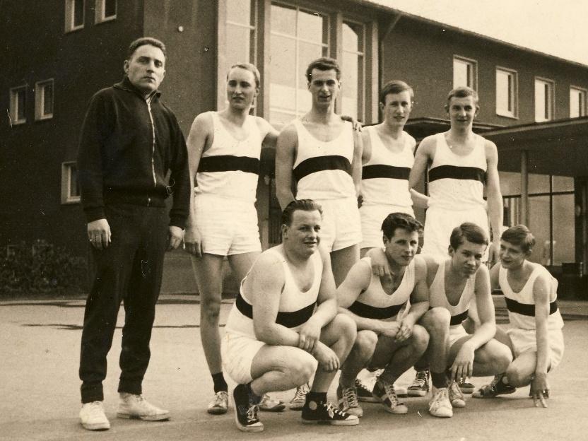 Gruppennfoto von neun Athleten in Sportkleidung, aufgenommen vor einem Gebäude, datiert 1962-63.
