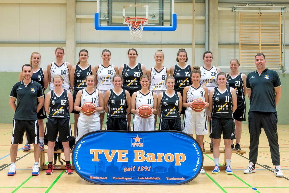 1. Damen 2021 Mannschaftsfoto einer Basketball-Mannschaft mit Spielerinnen in schwarzen und weißen Trikots vor einem Korb.