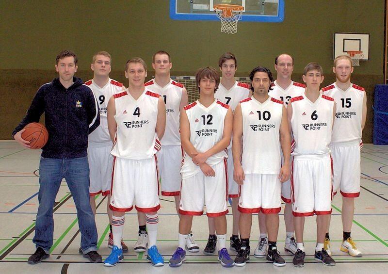 1. Herren 2011/12 Basketballmannschaft mit Trainer in Sportkleidung steht in einer Halle, Basketball in der Hand des Trainers.