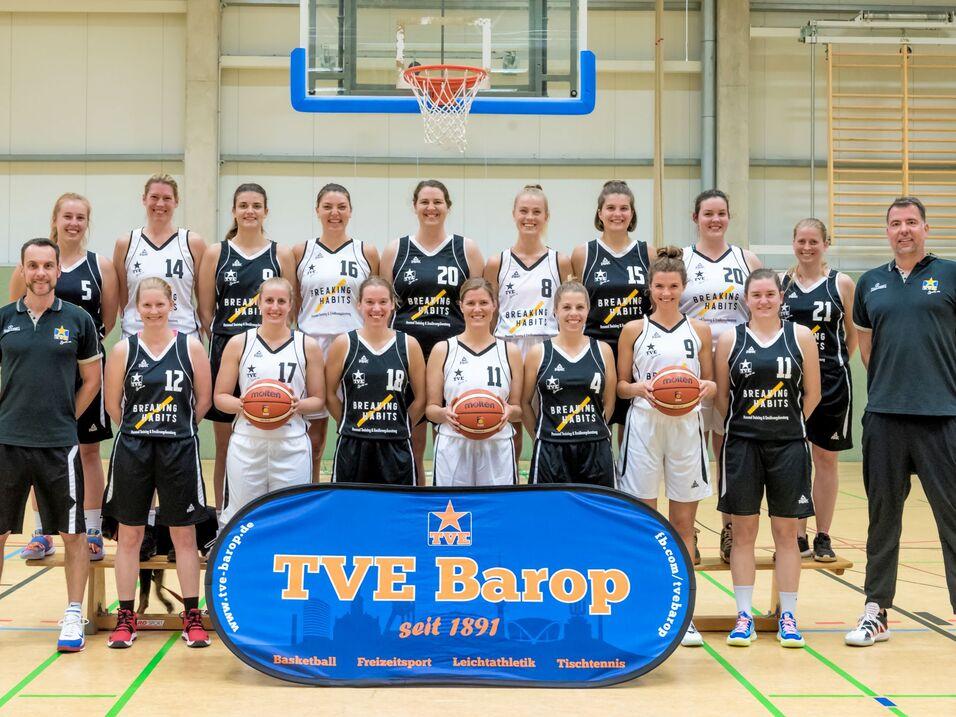 1. Damen 2021 Mannschaftsfoto einer Basketball-Mannschaft mit Spielerinnen in schwarzen und weißen Trikots vor einem Korb.