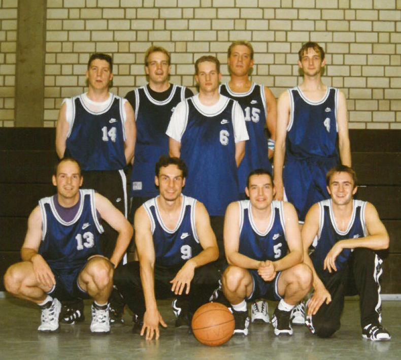 Herren 1998 Gruppe von Basketballspielern in blauen Trikots, posierend mit einem Basketball in einer Sporthalle.