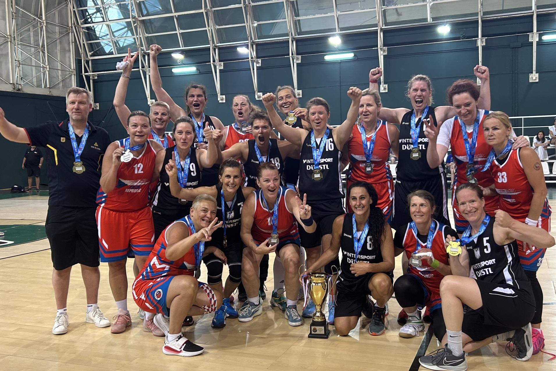 Gruppenvorstellung von Basketballspielerinnen mit Medaillen und Pokal auf dem Spielfeld nach einem Sieg.
