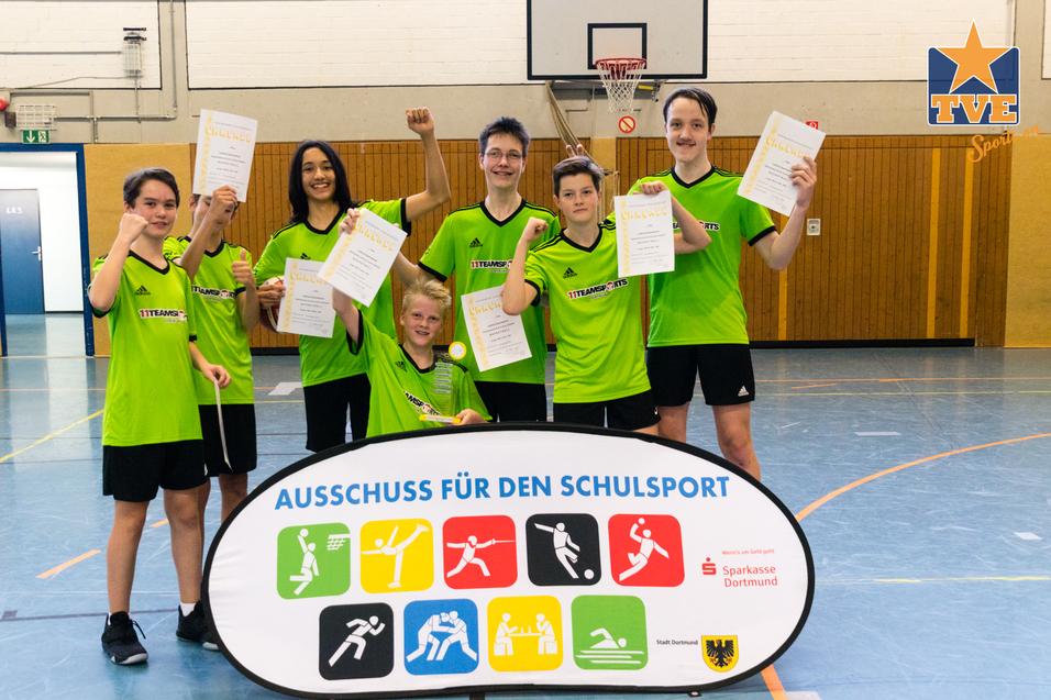 Sechs sportlich gekleidete Jugendliche stehen vor einem Banner zum Schulsport und halten Dokumente in den Händen.