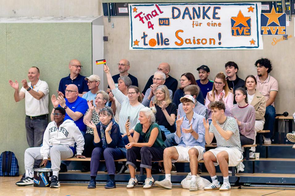 Gruppe jubelnder Zuschauer auf Tribüne mit Banner „Danke für eine tolle Saison“ in einer Sporthalle.