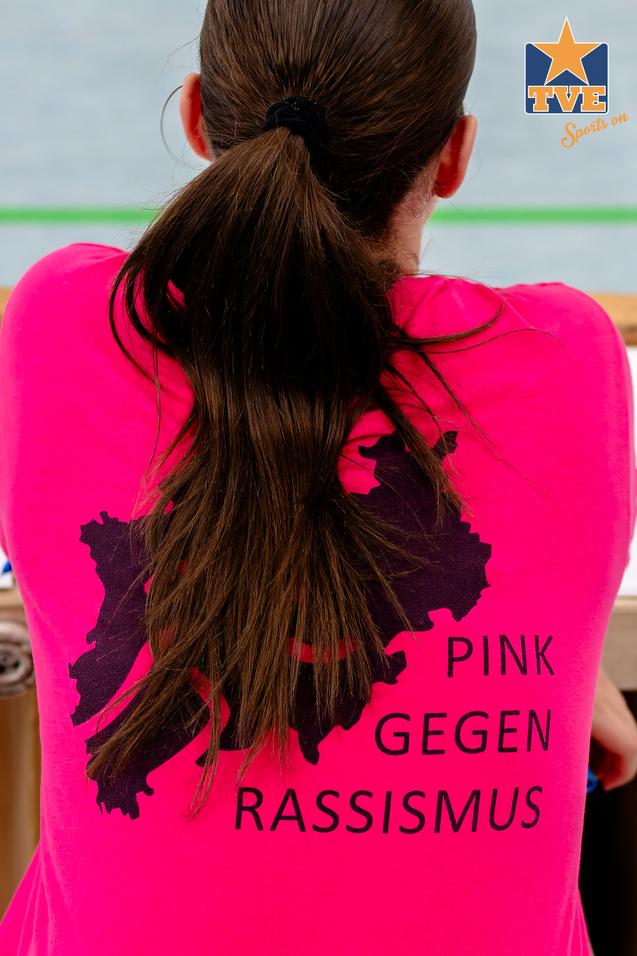 Integration Pink Rückansicht einer Person in pinkem Shirt mit dem Aufdruck „PINK GEGEN RASSISMUS“ und einer Landkarte im Hintergrund.