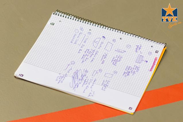Notizbuch mit handschriftlichen Skizzen und Notizen auf kariertem Papier, neben orangefarbener Linie.