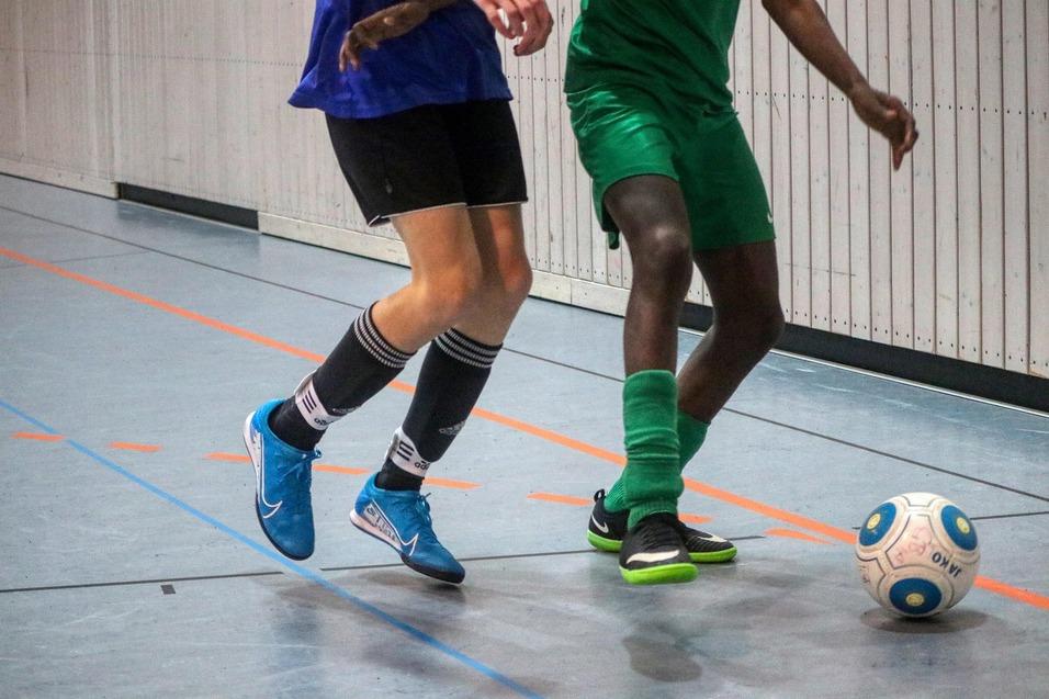 Nahaufnahme von zwei Spielern in Bewegung, die gemeinsam einen Fußball in einer Sporthalle spielen.