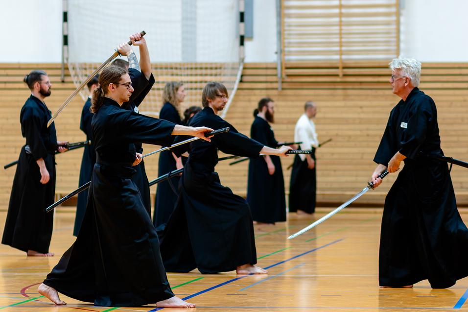Gruppenübung im Kendo mit Teilnehmern in schwarzen Gi, die mit Schwertern in einer Halle trainieren.