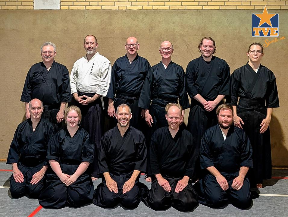 Gruppennporträt von elf Personen in traditionellen Schwarz-Kimonos, auf einem Sportboden stehend und um einander herum.