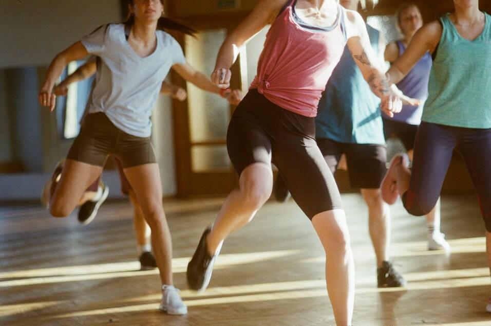Gruppe von Menschen in Sportkleidung, die im Fitnessraum synchron tanzen und sich energisch bewegen.