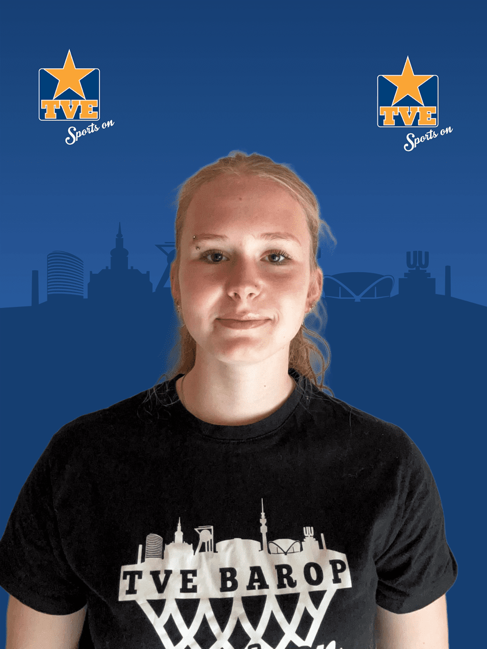Porträt einer Person mit blonden Haaren, die ein schwarzes T-Shirt mit „TVE BAROP“ trägt, vor blauem Hintergrund.