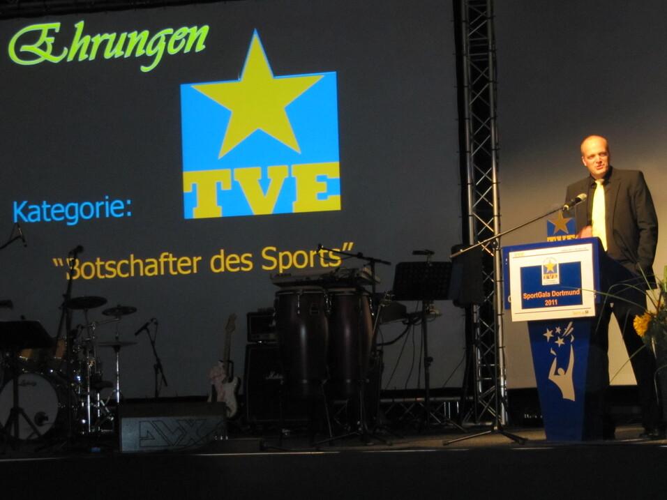Mann spricht auf Bühne bei Ehrungsveranstaltung, im Hintergrund Plakat mit der Aufschrift "Botschafter des Sports".