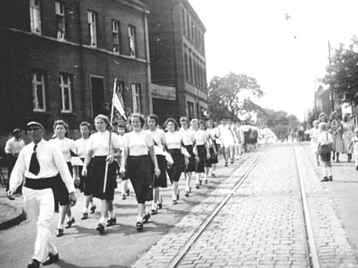 Historisches Schwarzwei&szlig;bild einer Damenparade mit Fahne in einer Stadtstra&szlig;e. Frauen tragen &auml;hnliche Kleidung und marschieren.